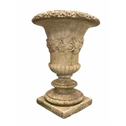 Well weathered composition stone urn of classical design, with egg and dart rim, floral bouquets to body, raised on circular stepped socle and square base H64cm