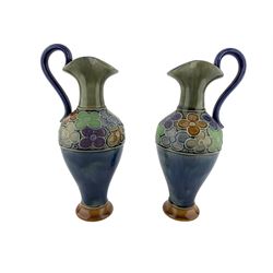 Pair of Royal Doulton stoneware ewers possibly by LF Bowen, with flared and pinched rim, scroll handle and a band of tubelined flowers to the shoulder, H22.5cm
