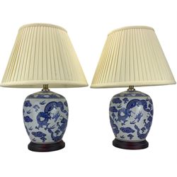 Pair of blue and white ovoid form table lamps, each decorated with dragons chasing the flaming pearl amidst clouds, raised upon circular hardwood bases, H28cm excluding fitting