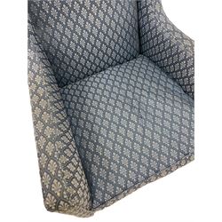 Edwardian wingback armchair, sprung back and seat upholstered in foliate patterned blue fabric, raised on mahogany tapered supports terminating in ceramic castors 