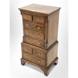 Reproduction figured walnut miniature tallboy, half sawn veneered and cross banded top over two short and three long drawers enclosed by canted and fluted sides, two short and one long drawer under, raised on bracket supports, W38cm, H77cm, D29cm