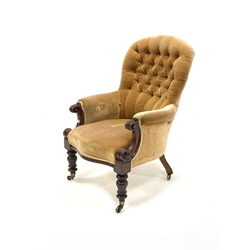 Late Victorian walnut upholstered armchair of generous proportion, covered in buttoned yellow velvet, with scroll carved arm terminals, raised on turned front supports with brass cup castors, W72cm