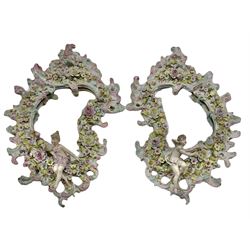 Pair of Ruldolstadt Volkstedt porcelain wall mirrors, scroll form with bevelled glass plates, the frames encrusted with flowers and Putti,  H49cm x W31cm