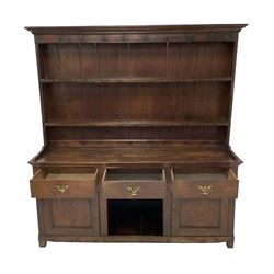 George III oak dresser, projecting cavetto cornice over two-tier plate rack and hooks, fitted with three drawers over two panelled cupboard doors flanking central recess, raised on stile feet