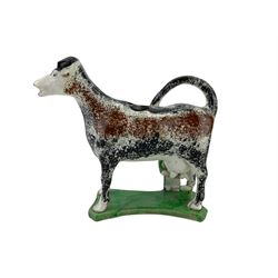 Early 19th century creamware cow creamer, probably Yorkshire, with curled tail handle, a milkmaid seated to one side with pail, decorated with sponged black and brown and set concave base, painted in green, L17cm x H15cm