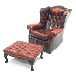 20th century wing back armchair, upholstered in deep buttoned and studded oxblood leather, raised on compressed bun supports and castors (W90cm), with rectangular footstool upholstered in deep buttoned oxblood leather (67cm x 50cm)