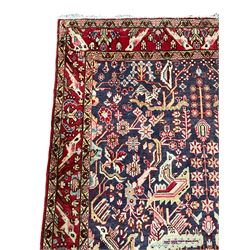 Persian indigo and crimson ground rug, the busy field filled with various bird and camel motifs surrounded by stylised plant designs, the guarded border with repeating bird and floral sequences 