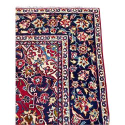 Persian red ground Kashan rug, the field with indigo central medallion surrounded by trailing and interlaced branches with stylised flower head motifs, guarded border with repeating floral design