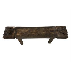 African Carved hardwood bench, the top carved with a spiral border flanked by stylised masks, raised on splayed supports
