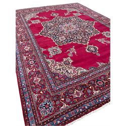 Large Persian Meshed red ground carpet, the plain field with large shaped central panel decorated with floral motifs, projecting stylised flower head medallions, the border decorated with repeating and scrolling stylised plant motifs