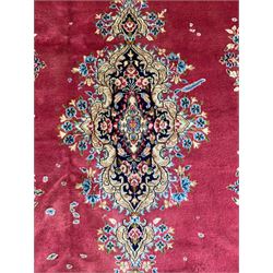 Persian Kerman red ground rug, the plain field with shaped floral medallion enclosed by a series of floral scrolls, the extending borders decorated with scrolling foliage branches and flowerheads
