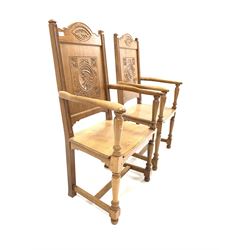 Pair of oak open armchairs, crest rail with incised carved detail over panelled back rest with further decorative carving, swept open arms, raised on turned and block supports united by stretcher W57cm