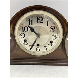 An early 20th century German mantle clock in a mahogany veneered Tambour case with mother of pearl inlay and satinwood banding, with a silvered dial, Arabic numerals and minute track, steel spade hands enclosed withing a convex glass and spun brass bezel, eight-day movement striking the hours and chiming the quarters on five gong rods. No pendulum or key.