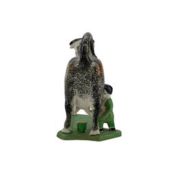 Early 19th century creamware cow creamer, probably Yorkshire, with curled tail handle, a milkmaid seated to one side with pail, decorated with sponged black and ochre and set concave base, painted in green, L17cm x H15cm