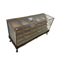 Early 20th century oak framed haberdashery shop counter, glass panel exterior enclosing sixteen graduating drawers with oak fronts and handles, raised on cabriole supports