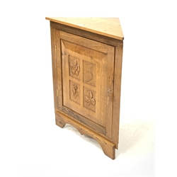 Yorkshire oak floor standing corner cupboard, with sngle fielded panelled door carved with floral decoration, enclosing one shelf, raised on shaped plinth base 