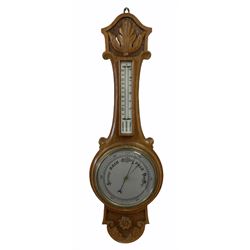 An English 1930’s solid oak carved hall barometer in a scroll shaped carved case with applied floral and leaf carving, compensated Aneroid movement, eight-inch silver painted dial measuring barometric air pressure from twenty-six to thirty-one point nine inches, weather predictions written in black upper and lower case gothic script with a blue steel indicating hand and brass recording hand, brass dial bezel with flat bevelled glass, mercury thermometer enclosed in a glazed rectangular box recording temperature in degrees Fahrenheit and Celsius on a white porcelain register, dial inscribed “Made in England”