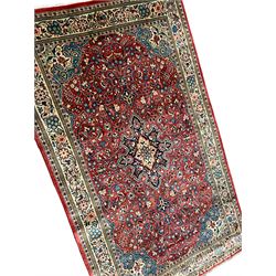 Persian Mahallat crimson ground rug, the densely decorated floral field with a central pole medallion, the curled indigo spandrels with palmette motifs, enclosed by an ivory border decorated with repeating foliate designs and stylised plant motifs