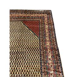 Persian Araak carpet, light ground field decorated with repeating small Boteh motifs, contrasting red ground spandrels, eleven band border decorated with geometric and stylised motifs