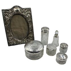 Embossed silver upright table photograph frame with oval aperture 12cm x 9cm Birmingham 1912, five glass dressing table jars with silver covers and a scent bottle