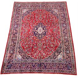 Large Persian red ground carpet, blue and ivory floral medallion on busy red field, with stylised foliate to triple guarded border 390cm x 294cm