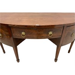George III mahogany demi-lune sideboard, the crossbanded top over three drawers and flanking cupboards, the facias with figured panels and foliage cast gilt metal handle plates, on square tapering supports with spade feet