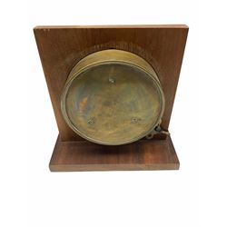 20th century circular brass cased clock with a twin train spring driven movement in the style of a bulkhead clock, 17.78 cm diameter brass case with a 15.24 cm diameter brass bezel, 12.7 cm diameter white paper dial with Roman numerals and minute track, spade hands and second hand, housed in a mahogany display stand, with key.