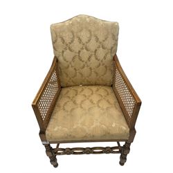 Early 20th century beech framed bergere armchair, shaped back with cane arm supports, sprung seat and back upholstered in ivory damask fabric, on turned supports with flower head carved front stretcher (W53cm H89cm); Early 20th century hall chair, high back over cane seat (W39cm H91cm)