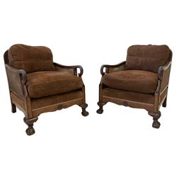 Pair early 20th century walnut bergère armchairs, the back and arms with double cane panels, the shaped backs carved and applied with foliate and shell decoration, upholstered in chocolate corduroy fabric with sprung seat and loose cushions, raised on cabriole supports with ball and claw feet