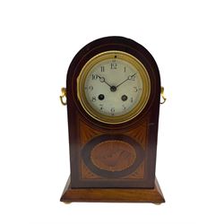 A decorative early 20th century French mantle clock in a round topped mahogany case with inlaid satinwood stringing and a contrasting oval and fan inlay to the front, white enamel dial with finely painted Arabic numerals and minute track,  matching steel moon hands within a decorative cast bezel and convex glass, eight-day French going barrel movement striking the hours and half hours on a coiled gong. With pendulum. 



