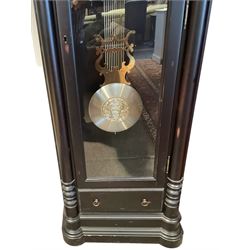 German - Hermle 'Nicolette' contemporary 8-day chiming longcase clock, ebonised case with a flat topped pediment and deep cornice, fully glazed door displaying three silvered case weights and a gridiron pendulum, on a stepped and moulded plinth with sliding draw, two part metal dial with a gilt bezel, pierced decoration to the centre and a silvered chapter, gilt Arabic numerals and contrasting steel hands, Hermle three train movement chiming the quarters and hours on two banks of 12 gong rods, with silent and chime selector playing Whittington, St Michael and Westminster chimes.
With winding key, three weights and pendulum.