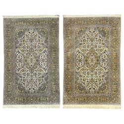 Pair Persian Kashan ivory ground rugs, all-over scrolled and interlacing foliate design with stylised plant motifs, central floral medallion and matching spandrels, the guarded border decorated with trailing foliage design