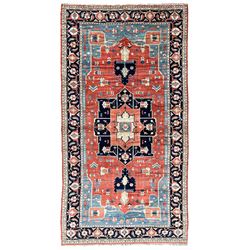 Large Persian Heriz carpet, red ground with geometric star medallion, surrounded by angular vine and geometric motifs, blue ground guarded border band decorated with a series of stylised flower heads and trailing foliate