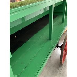 Florists market hand drawn barrow in green and red livery, the sloped top with shaped apron over four simulated grass covered staggered tiers and storage well, cast iron leaf suspension and iron bound twelve spoke wheels, L290cm