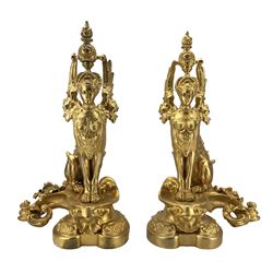 Pair of ornate gilt metal fire dogs in the form of Sphinxes, raised on scroll bases, H54cm