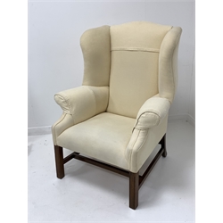 George III style mahogany framed wingback armchair, upholstered in natural linen, with shapely swept wings and arm rests, raised on square moulded front supports with stretchers 
