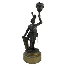 19th century French bronze candlestick modelled as a Knight, modelled as a standing wearing a plumed helmet and body armor, a shield in one hand and holding aloft a single sconce, on polished circular brass base, H27cm 