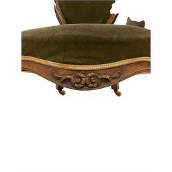 Victorian walnut open armchair, the cresting rail carved with flower heads and extending foliage, oval back with moulded frame, upholstered in green fabric, scrolled arm terminals on shaped supports carved with flower heads, cabriole front feet, on brass and ceramic castors