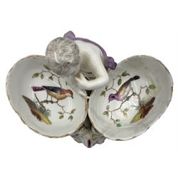 Pair of 19th century Berlin porcelain double salts, each modelled as a putto standing between two basket weave oval salts internally painted in polychrome enamels with exotic birds, and courting couples, raised upon three scroll supports, H12.5cm