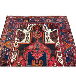 Persian Hamadan red ground rug, the field decorated with stylised plant motifs and geometric designs, the ivory spandrels with large Boteh motifs, the guarded indigo border with repeating geometric and bird motifs