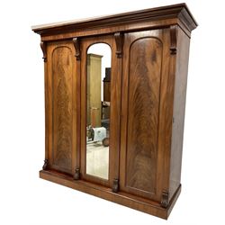 Late 19th century mahogany triple wardrobe, the projecting cornice over banded frieze, the central door with arched full length mirror flanked by two figured panelled doors, the uprights topped with reeded and scrolled corbels decorated with acanthus leaves, the interior fitted with coat hooks,  two hanging rails and two drawers, raised on plinth base 
Provenance: property of a gentleman