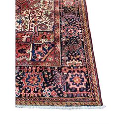 Persian Heriz crimson ground carpet, the field decorated with a central floral medallion surrounded by geometric stylised plant motifs with contrasting ivory spandrels, the multi-band border with repeating foliate patterns