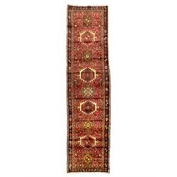 Persian Karajeh runner, red ground with nine geometric medallions, the field decorated all-over with small stylised plant, animal and bird motifs, the border decorated with geometric star motifs