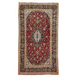Persian Kashan crimson ground rug, the central pole lozenge medallion surrounded by all-over interlacing floral patterns, the heavily guarded indigo border with repeating palmette motifs connected by trailing leafage