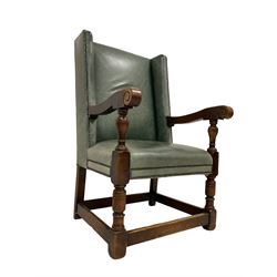 Early 20th century oak framed wing back armchair, upholstered in studded leather with sprung seat, the arms terminating in carved scrolls with turned front supports 