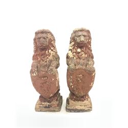 Pair of reconstituted stone garden lions, holding heraldic shields, raised on a stepped square base, with remnants of red primer paint H75cm