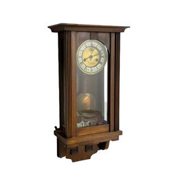 A late 19th century German spring driven wall clock in a mahogany case, with a flat top and full-length round topped glazed door, eight day striking movement, striking the hours and half hours on a single gong rod, two-piece dial with a gilt centre and enamel chapter ring, roman numerals, minute track and pierced steel hands within a pressed brass bezel. With pendulum and key.



