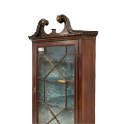 Edwardian mahogany corner cabinet, dentil broken swan neck pediment over astragal glazed door, the lower cupboard enclosed by panelled door with shell inlay, on shaped and bracketed plinth base 