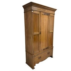 Arts & Crafts style oak wardrobe, the projecting cornice over one panelled door, opening to reveal interior fitted for hanging with one interior mirror over one drawer and shaped apron