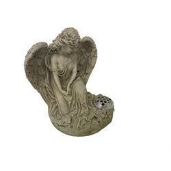 Composite stone garden ornament or memorial statue in the form of a Classically draped winged angel kneeling, on a naturalist base with flowers